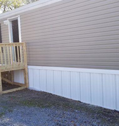 Exterior of a tan mobile home with white skirting and wooden entry steps
