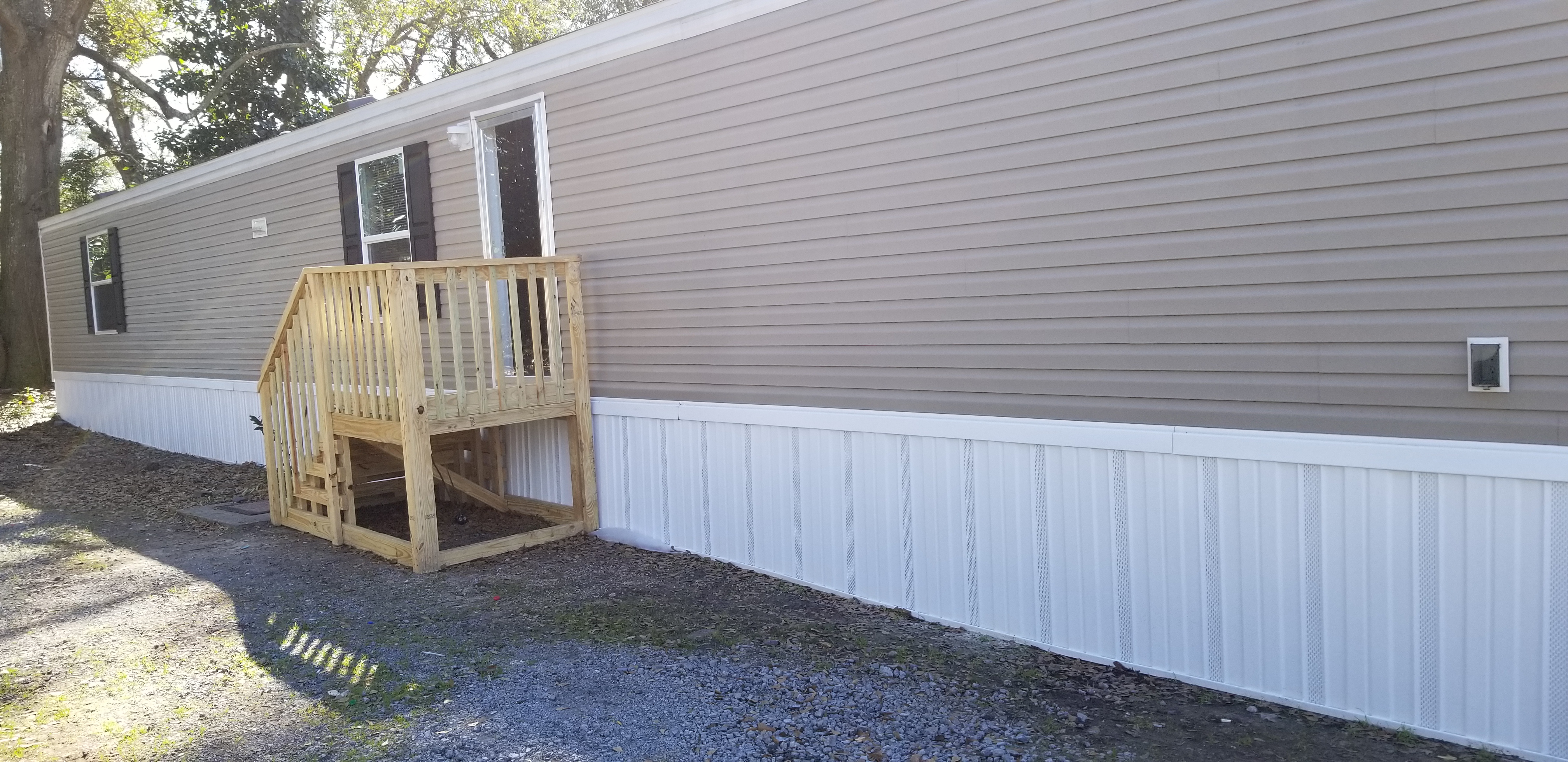 Exterior of a tan mobile home with white skirting and wooden entry steps